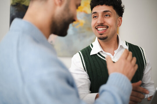 Two men are engaged in a conversation, one smiling broadly while the other gestures with his hand.