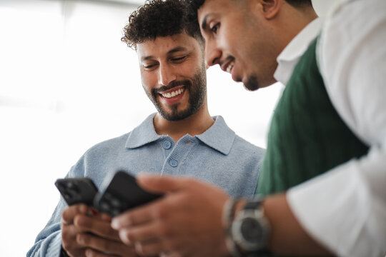 Two young men share a moment of connection as they look at a mobile phone together, smiling and engaged in conversation.