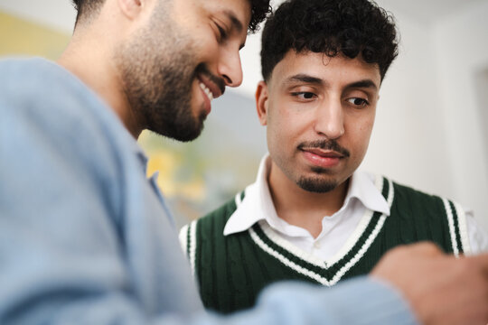 Two young men share a moment of connection, one smiling warmly as they look at something together.