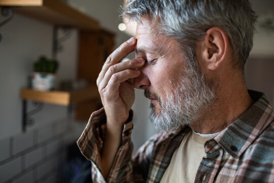 Worried senior man with headache in home kitchen
