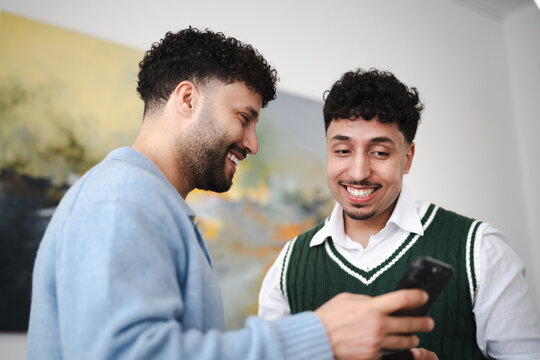 Two young men share a laugh while looking at a smartphone together, showcasing connection and shared digital experiences.