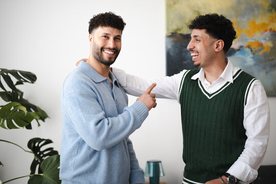 Two young men share a laugh and a friendly gesture, one with his arm around the other's shoulder, in a bright, modern indoor setting.
