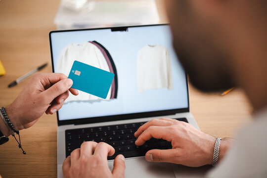 A person uses a debit card to make an online purchase of clothing on a laptop.