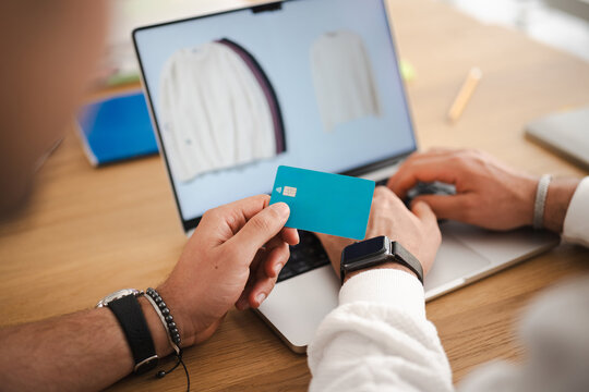 A person holds a debit card while shopping online on a laptop, showcasing a modern and convenient way to make purchases from home.