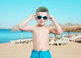 Fototapeta premium Adorable little boy in swimwear with sunglasses on beach