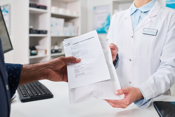 Close up of pharmacist handing prescription pickup package to middle aged man at pharmacy counter, showing medication dispensing and patient service for healthcare marketing © pressmaster