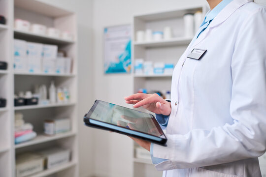 Close up of middle aged woman healthcare worker using tablet in pharmacy, managing inventory and patient records. Ideal for medical technology, digital healthcare, clinic workflow