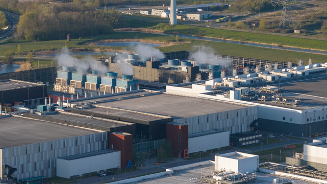 Aerial view of the Google Data Center featuring cooling towers with steam and modern industrial buildings surrounded by green fields in Eemshaven, Groningen, Netherlands.