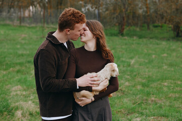 Obraz premium Happy couple in a countryside field cuddle a young goat kid, sharing tender smiles and hands on the small animal, capturing warm lifestyle moment with gentle farm charm.