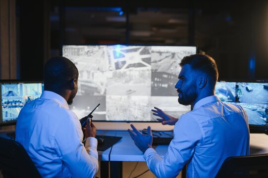 Two security guards sitting by workplace in front of monitors and observing cctv video