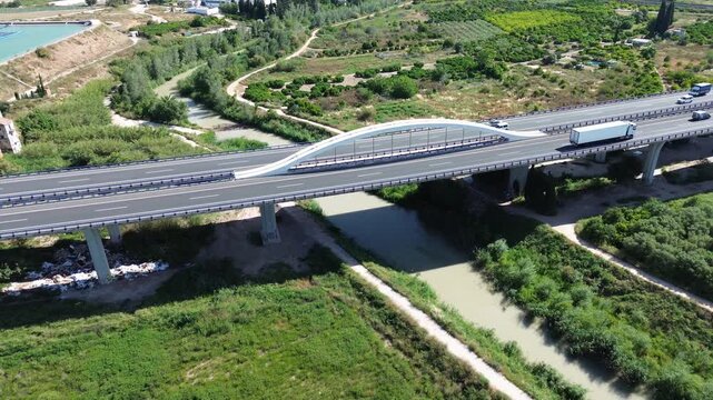 Aerial view of the A7 Autovia del Mediterraneo highway bridge crossing the Rio Segura in Murcia Spain with heavy truck traffic flowing over fertile green agricultural crop fields, orchard and nature