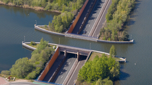 Aerial view of the Aquaduct Veluwemeer with cars driving through the tunnel under the water surface surrounded by lush green trees in Harderwijk, Gelderland, Netherlands.