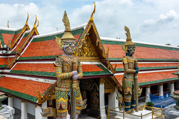 Obraz premium Pair of Yaksha guardian statues in front of Wat Phra Kaew roofs, Bangkok