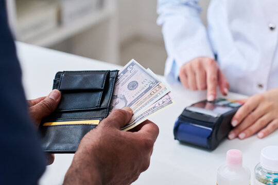 Close up of middle aged man holding wallet and cash while pharmacist processing card terminal payment at counter, showing healthcare purchase and pharmacy checkout use in retail health marketing