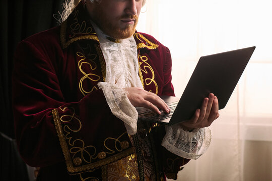 young man wearing historical costume using laptop, blending past era styling with modern technology. Ideal for digital transformation, innovation, contrast, medium shot