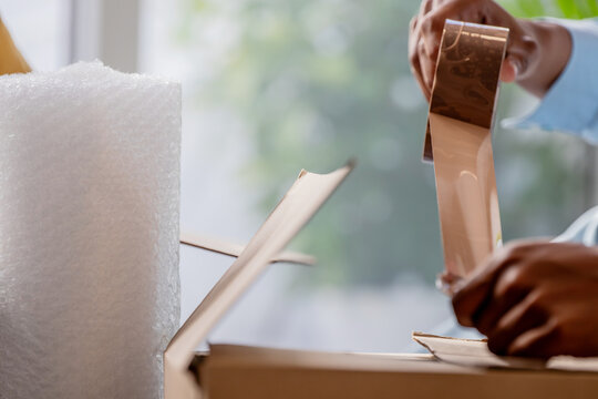 Person sealing a cardboard box with packing tape and bubble wrap, preparing shipment or moving belongings. Perfect for logistics, e-commerce and relocation concepts