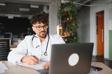 Arab doctor attending online meeting and taking notes on clipboard