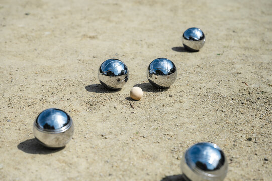 Detailed view of petanque court with scattered steel balls on textured sand and gravel, outdoor boules game equipment