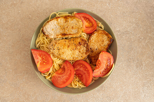 Top view of grilled pork steaks with spaghetti pasta and fresh tomato slices for home cooking recipe and food delivery menu