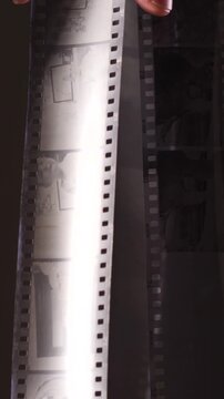 Vertical video hands examining a strip of developed 35mm film negative, showcasing the analog photography process and the tangible result of traditional darkroom developing