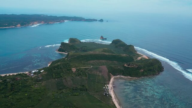Aerial Green Island Cape With Curved Beaches, Rolling Hills And Farmland Pockets, Long Reef Line Shaping Waves, Secluded Bays, Turquoise Shallow Water Meeting Deep Ocean, Katil beach,Lombok,Indonesia