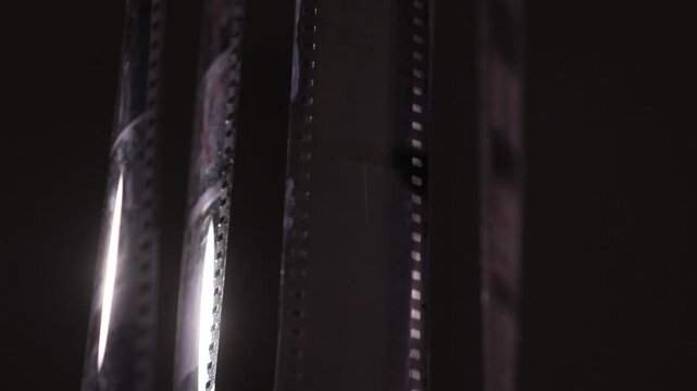 Film strips hanging vertically, revealing the negative images and perforation holes, representing the traditional process of cinema and analog photography development