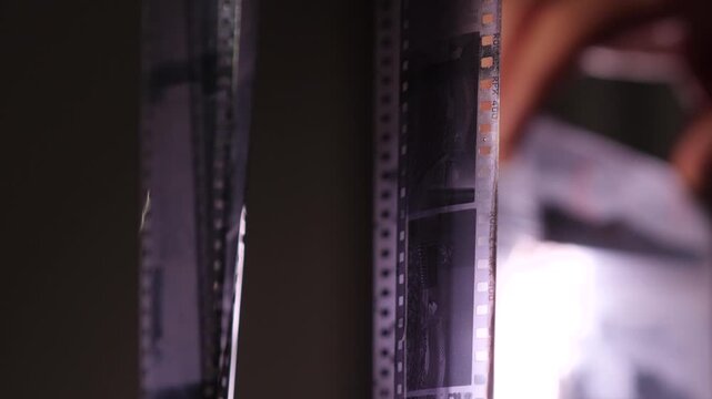 Photographer developing black and white film negatives, hanging wet strips of 35mm film during a traditional analog reproduction process focused on the art of darkroom photography