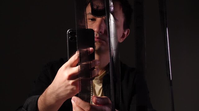 Man holding a film strip, using a smartphone to digitize and convert analog photographic negatives into digital images in a modern fusion of classic and contemporary technology