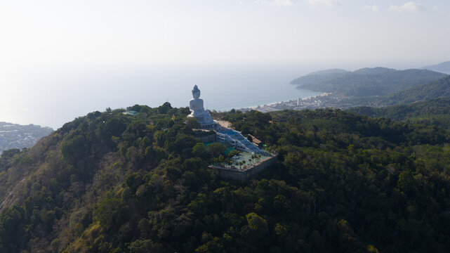 Aerial view of the Big Buddha Phuket statue situated on a lush green hilltop overlooking the Andaman Sea coastline in Karon, Phuket, Thailand.