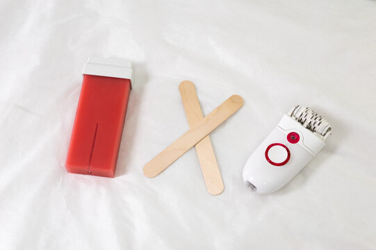 wax cartridge with wooden spatulas vs epilator on white background. Compact devices arranged for DIY home wax depilation prep. Clean minimal styling. concept of choosing between hair removal products