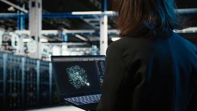 Data center female programmer using AI LLM model on laptop to optimize equipment rigs. Woman in server hub using large language model neural network technology to adjust system parameters