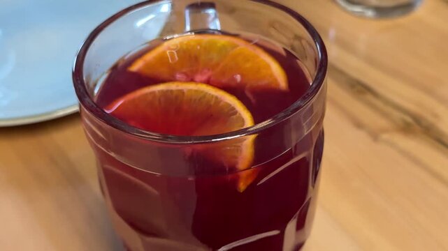Hot red berry compote or fruit tea made from raspberries and mixed red berries served in a large glass beer mug with fresh orange slices, warm cozy drink concept