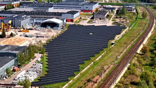 Aerial parallax around large solar panel farm beside railway tracks and industrial buildings in urban district of Jelgava, Latvia