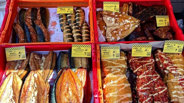Assorted smoked fish and seafood products displayed in market crates, featuring fillets, rolled cuts, and glazed specialties at a traditional food stall.