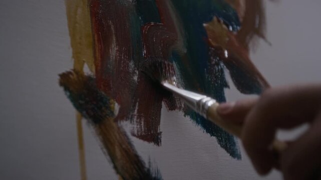 Extreme close up view of painters hand applying multicolored expressive strokes of oil paint with paintbrush, creating contemporary abstract artwork on canvas