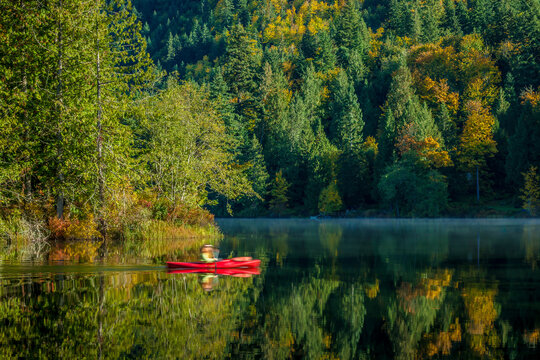 A woman paddles a red canoe on a calm still lake in autumn in northern Washington State