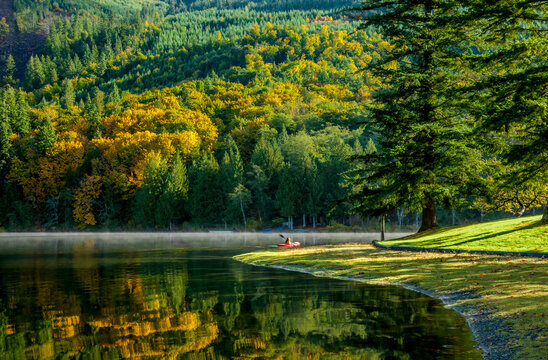 A woman paddles a red canoe on a calm still lake in autumn in northern Washington State