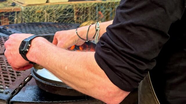 Street food vendor grilling mollusks over open flame at outdoor market stall