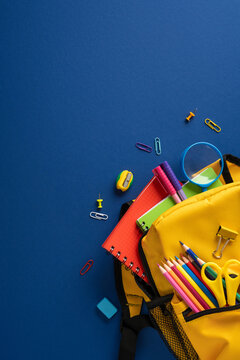 Back to school vertical essentials: yellow backpack with colorful stationery and notebooks on blue background