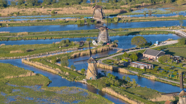Aerial view of historic windmills standing along blue canals surrounded by lush green fields and reeds Kinderdijk, South Holland, Netherlands.