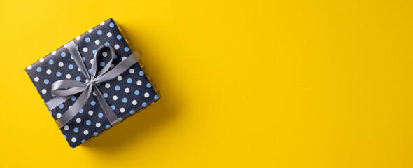 Obraz premium Happy Father's Day gift box with blue polka dot wrap and silver ribbon on yellow background