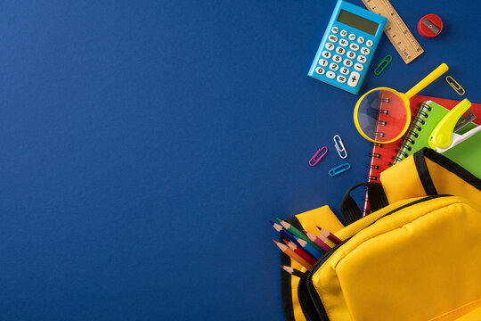 Back to school supplies with yellow backpack, colorful pencils and notebooks on blue background