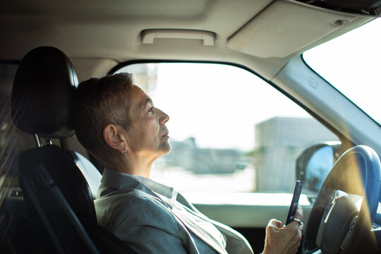 Side view of senior woman driver using smartphone in parked car