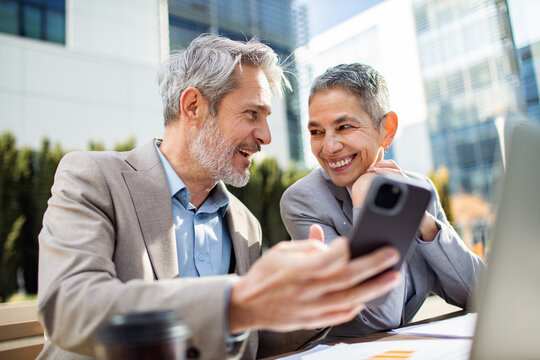 Senior business colleagues discussing smartphone outside office