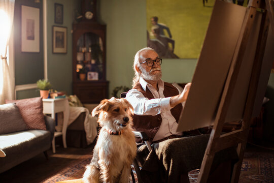 Elderly man painting at home with dog companion