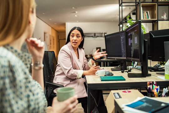 Two coworkers discussing project at dual monitors in modern office
