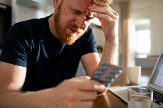 Stressed man with headache choosing pills at home office