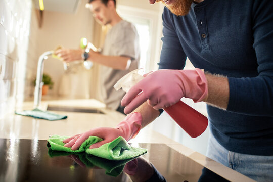 Two men cleaning kitchen countertop with spray bottles