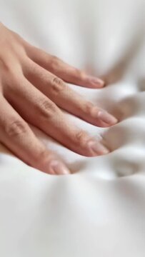 Vertical video: Placing single hand pressing and sliding on bed satin fabric, feeling texture