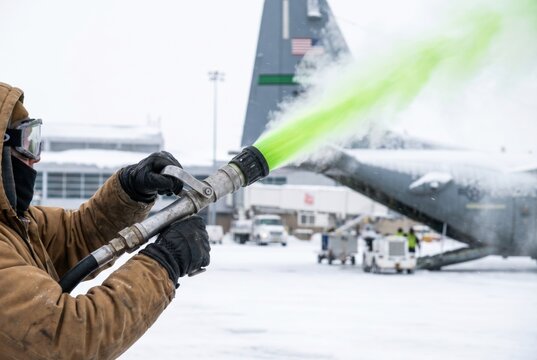 Aviation worker spraying bright green deicing fluid onto a large cargo airplane during winter